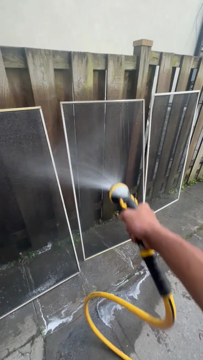 Window screens being rinsed with a hose